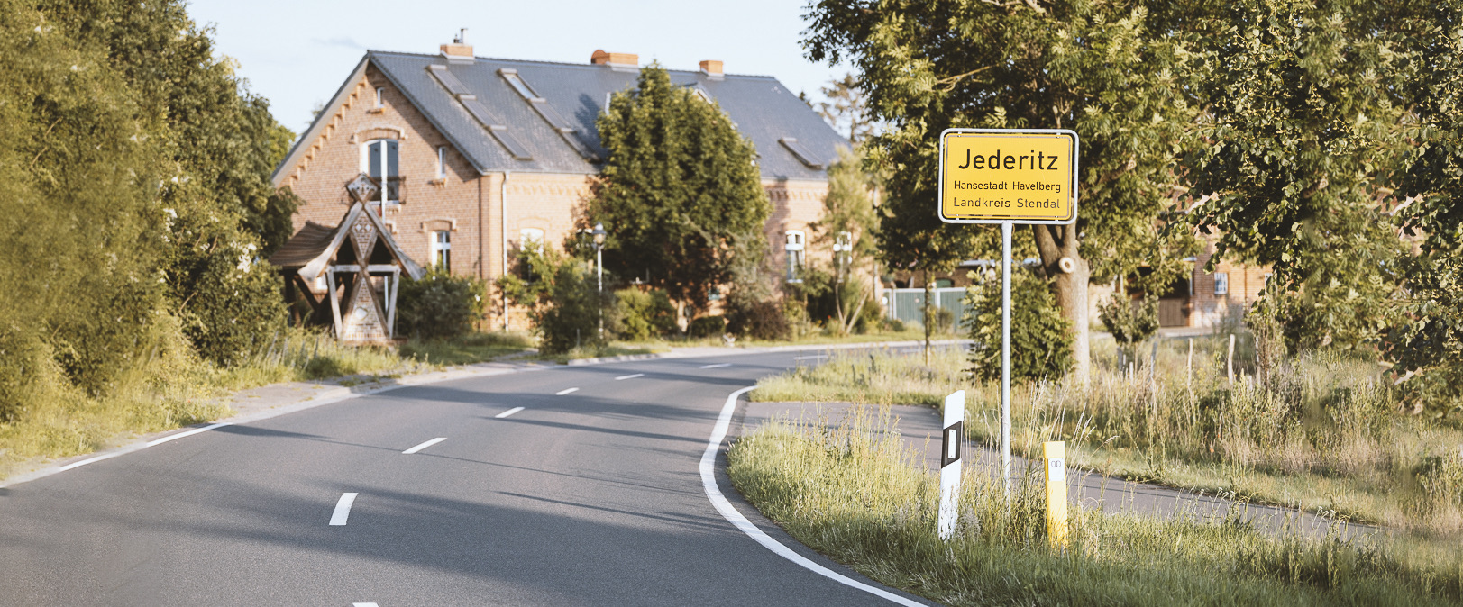 Ortseingang von Jederitz — Ortsschild an der Landstraße, dahinter das Backsteinhaus